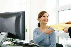 Woman sitting at desk accepting a letter to be mailed.